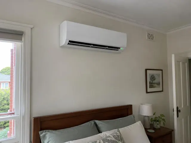 White split system above a bedroom bed on a pale wall, louvre open in a tidy home in Prospect