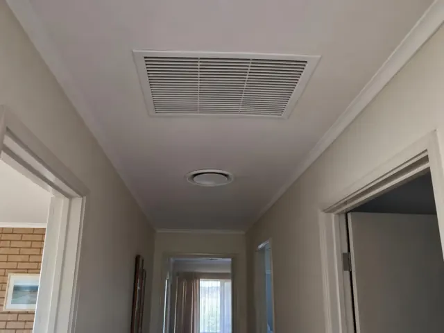 Ceiling return-air grille in a narrow hallway with white trim and beige walls in Clearview