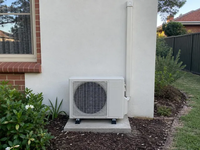 Outdoor split-system unit on a concrete pad beside a rendered wall and garden in Enfield