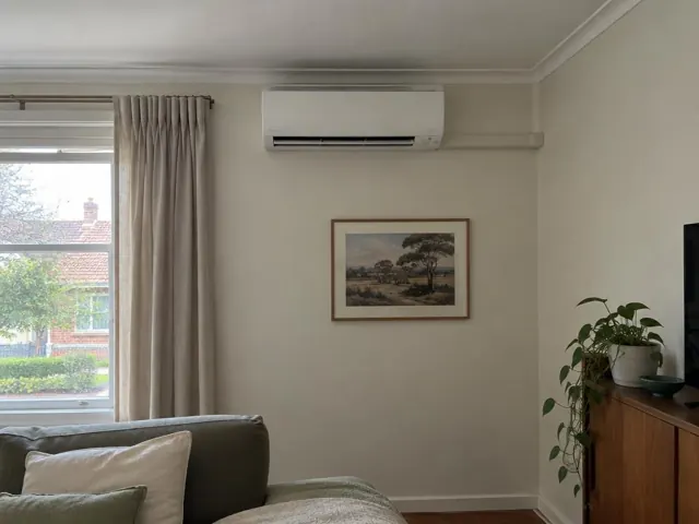 Indoor split system mounted high on a living room wall with curtains and framed art in Blair Athol